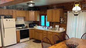A wooden kitchen with a dining table, chairs, and a refrigerator. - Charming 3-bdrms & loft cabin, with WiFi, mins to Elk Mountain by Lake Idlewild (Clifford)