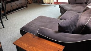 A cozy living room with a stone wall, a ceiling fan, a TV, and a balcony with curtains. - Charming 3-bdrms & loft cabin, with WiFi, mins to Elk Mountain by Lake Idlewild (Clifford)