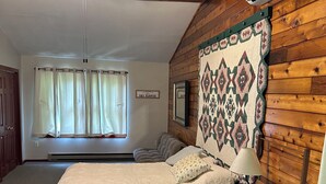 A bedroom with a wooden ceiling, a bed with a quilt, a nightstand with a lamp, and an air conditioning unit. - Charming 3-bdrms & loft cabin, with WiFi, mins to Elk Mountain by Lake Idlewild (Clifford)