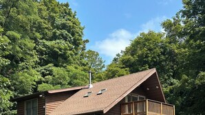 A log cabin with a deck and a chimney, surrounded by lush greenery. - Charming 3-bdrms & loft cabin, with WiFi, mins to Elk Mountain by Lake Idlewild (Clifford)