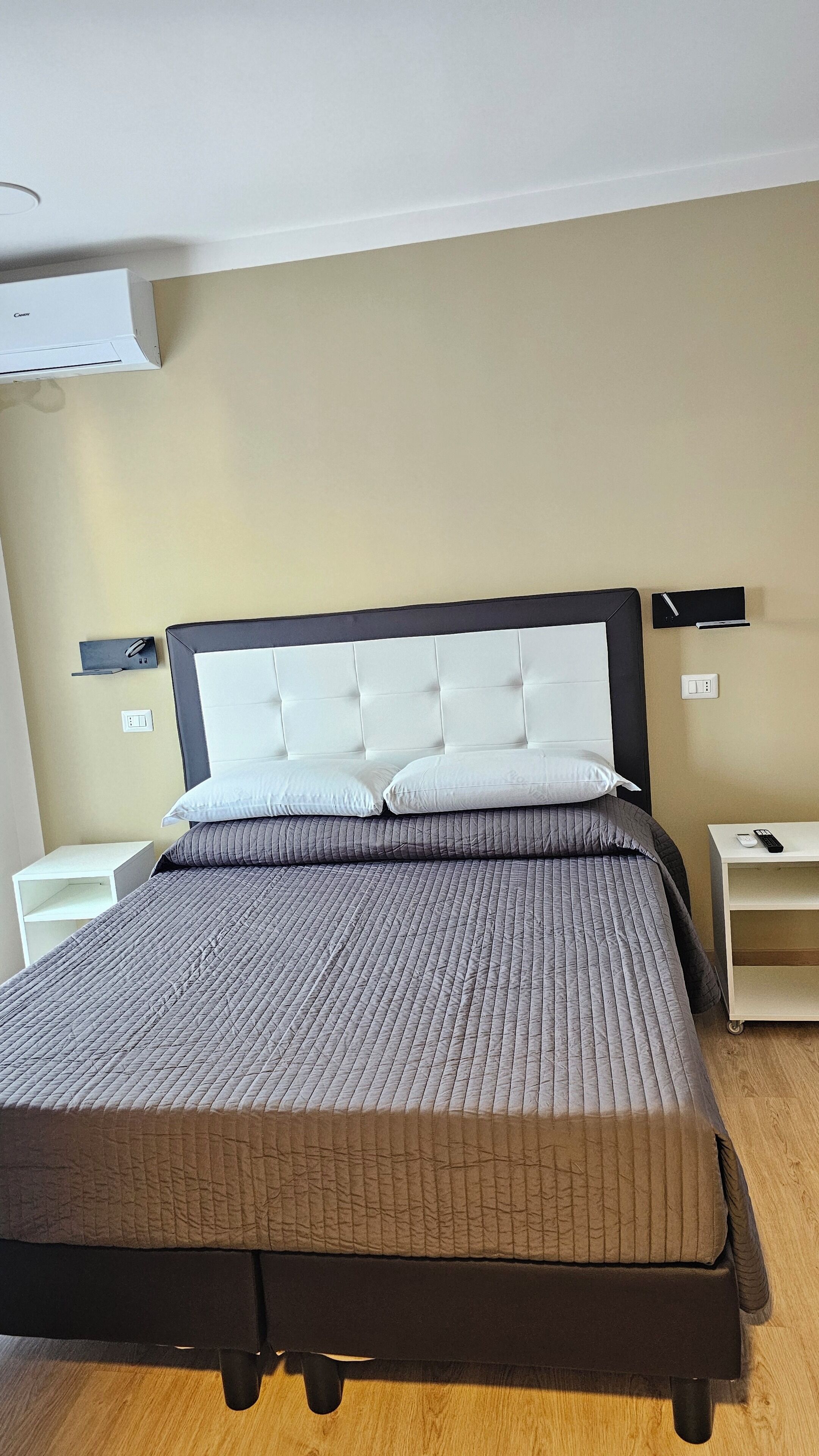 A neatly made bed with a quilted cover, a headboard with a tufted design, and a bedside table with a remote control.
