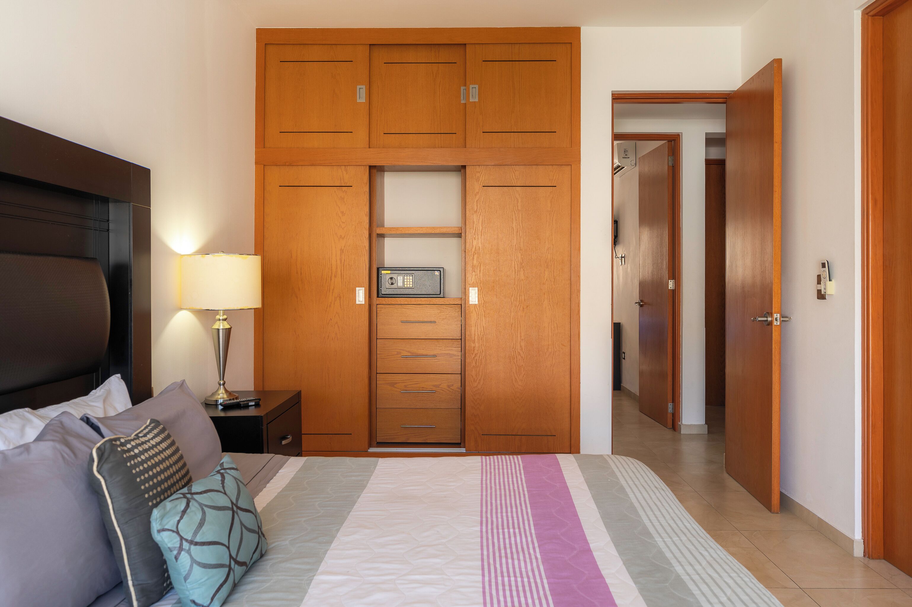 Een slaapkamer met een bed, nachtkastje, lamp, houten garderobe en een deur naar de badkamer.