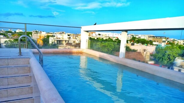 A rooftop swimming pool with clear blue water, a metal ladder, and a view of surrounding buildings. - Rooftop pool. Luxury apartment in Playa del Carmen (Playa del Carmen)