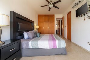Een slaapkamer met een bed, nachtkastje, plafondventilator, kledingkast en een televisie.