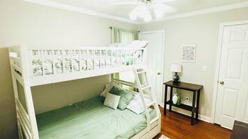 A bunk bed with a ladder, a small table with a lamp, a door, and a patterned rug.
