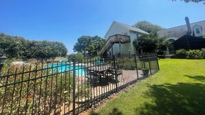 Un jardin avec une piscine, un patio clos et une maison dotée d’un balcon.