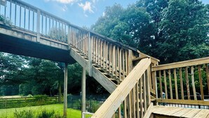 Un escalier extérieur en bois menant à une terrasse, entourée d’un jardin et d’arbres.