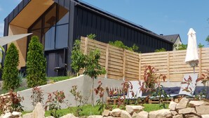 A modern building with a sloped roof, a wooden fence, and a stone wall in the foreground. - Modern chalet - relaxing stay with private spa, calm, nature and comfort (RUYNES EN MARGERIDE)