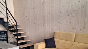 A modern living room with a wooden wall, a beige sofa, a black cushion, a marble-tiled floor, and a black metal staircase. - Modern chalet - relaxing stay with private spa, calm, nature and comfort (RUYNES EN MARGERIDE)