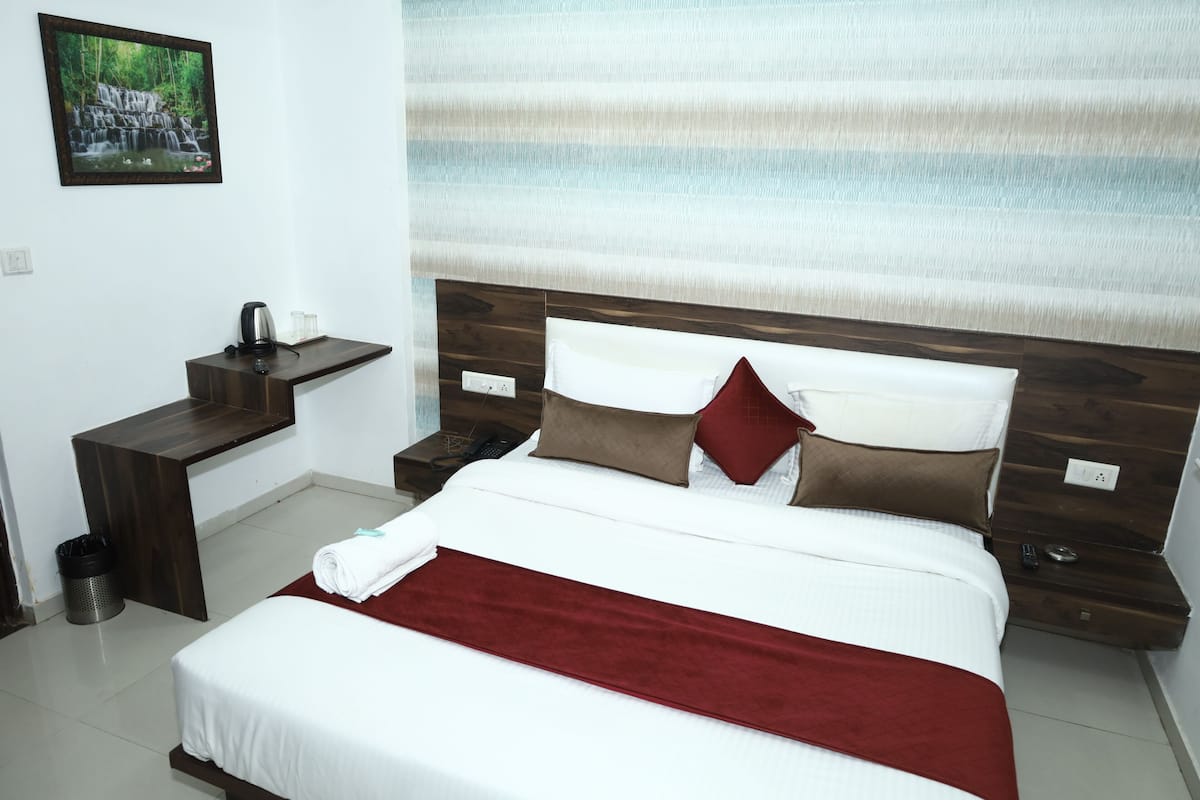 A neatly arranged hotel room with a bed, bedside tables, a nightstand, and a wall-mounted picture.