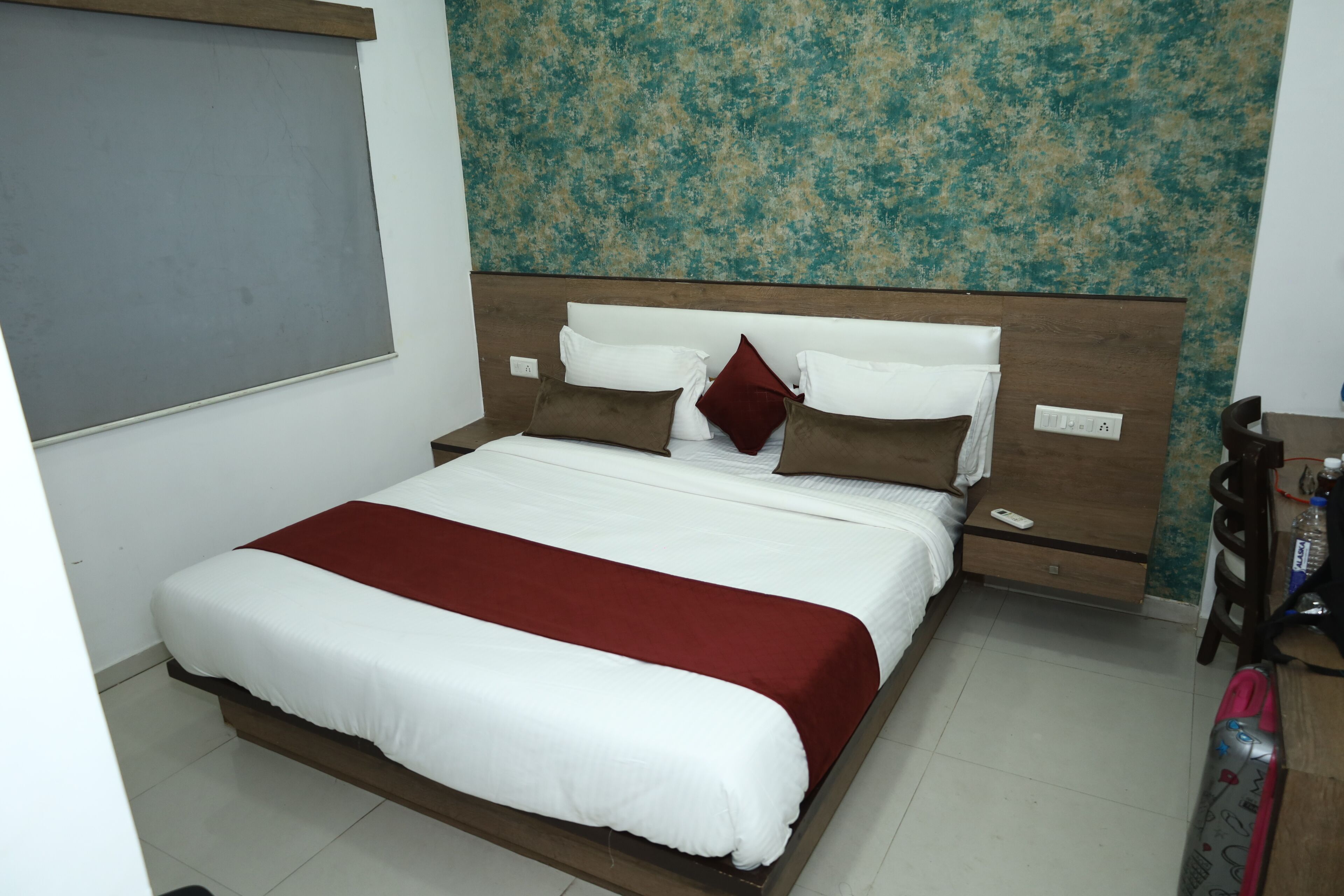 A neatly made bed with white and red bedding, a wooden headboard, and a wall with a textured pattern.