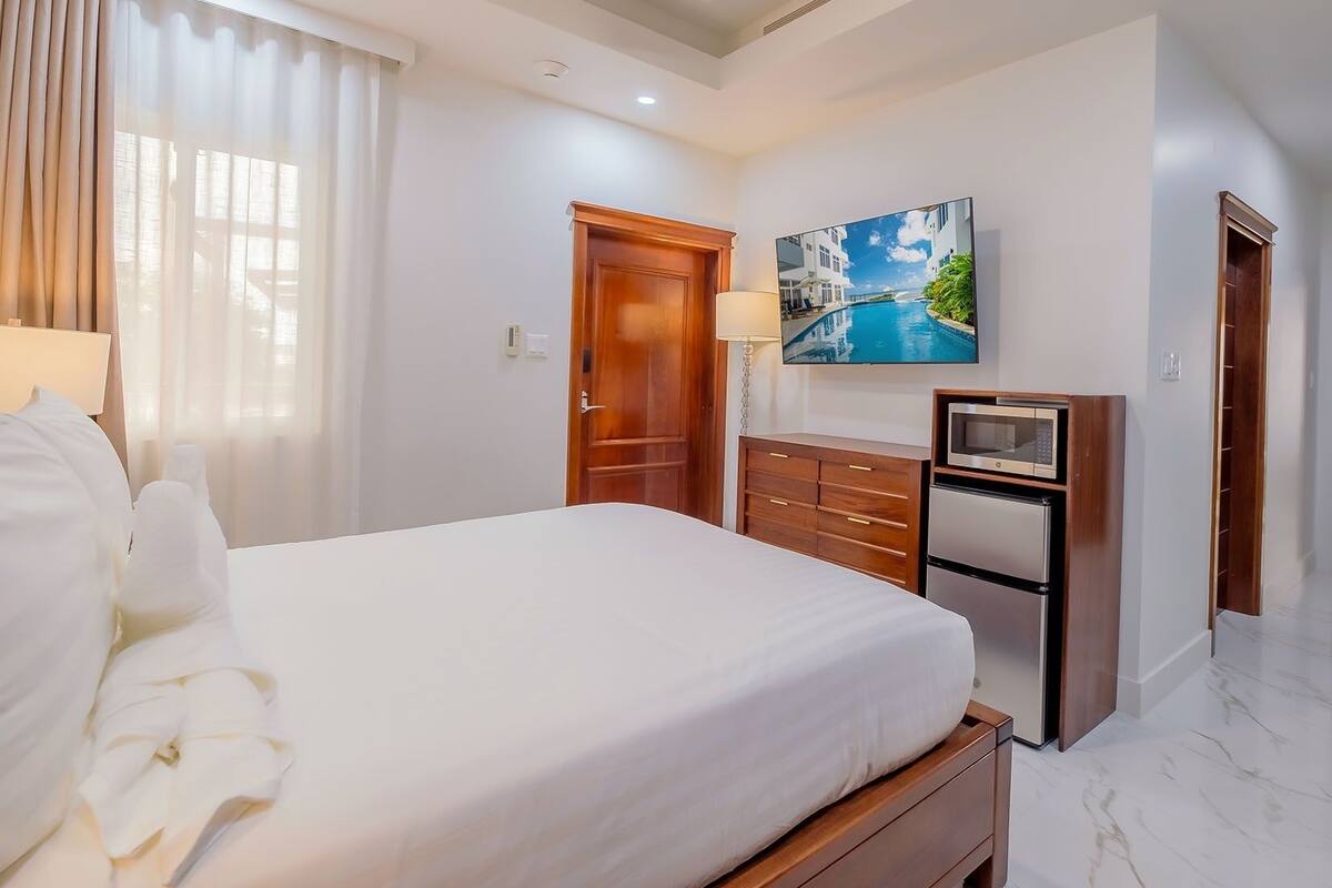Een hotelkamer met een groot bed, een flatscreen televisie, een houten dressoir en een schilderij van een kustlandschap.