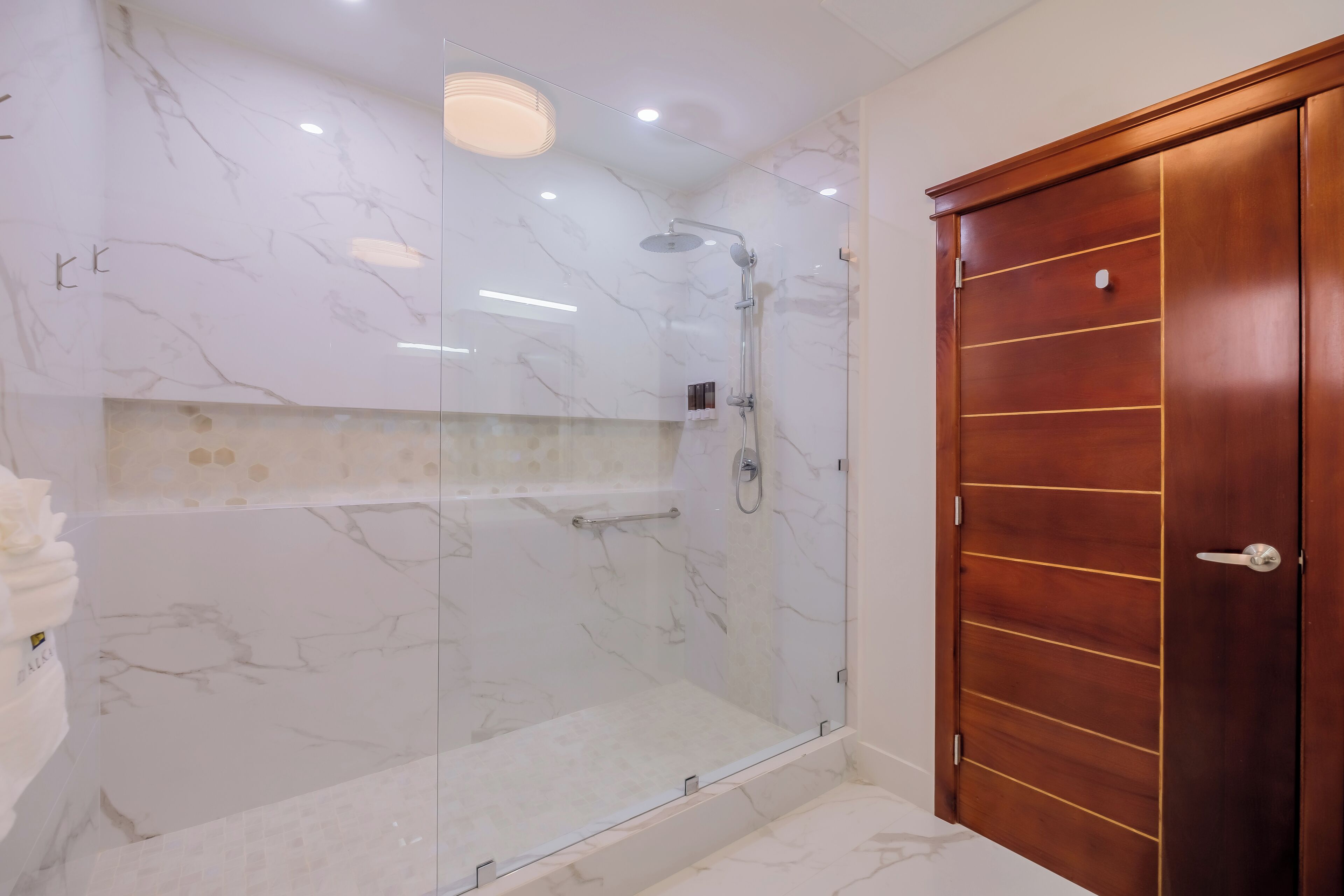 A modern bathroom with a glass-enclosed shower, marble walls, and a wooden door.