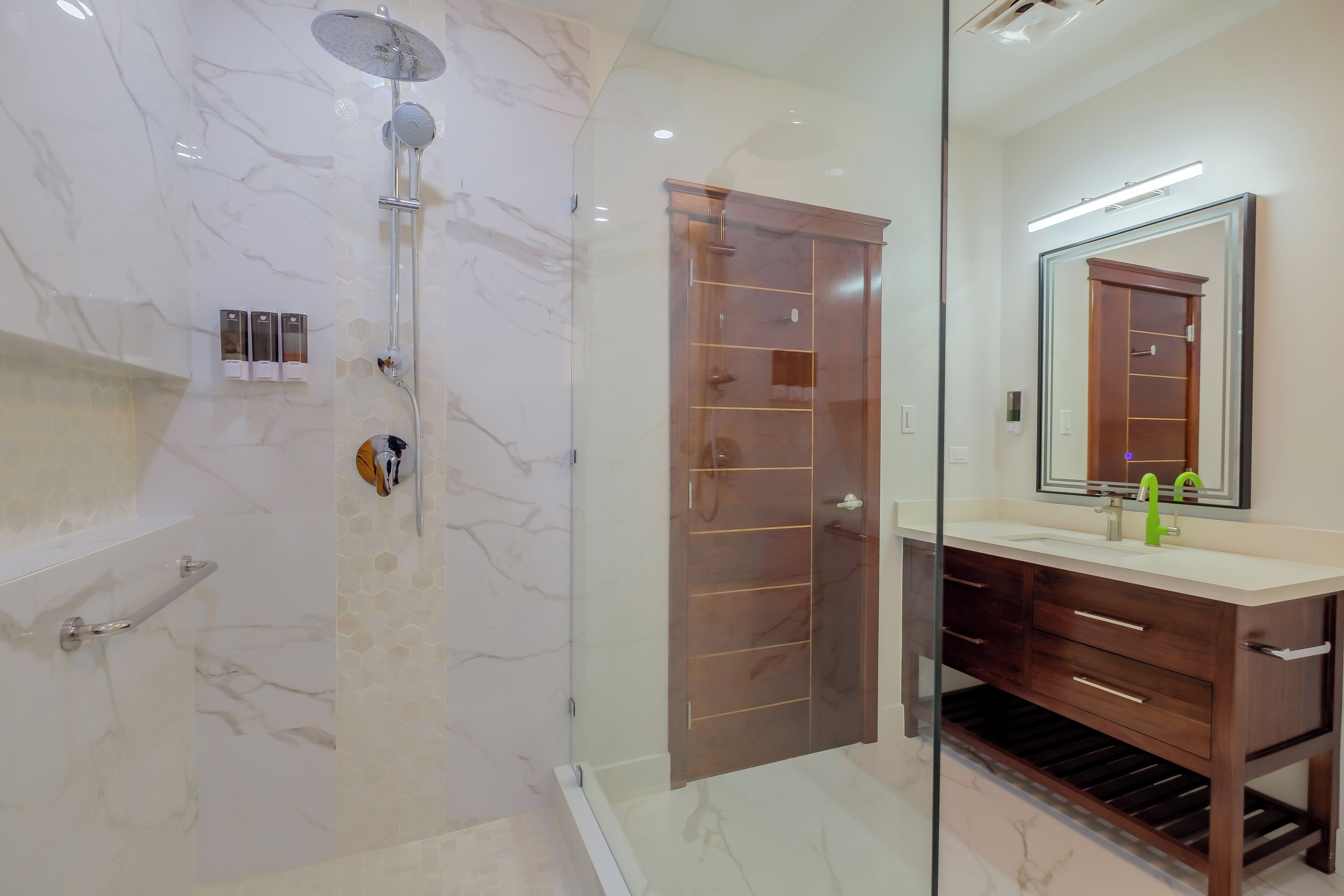 A modern bathroom with a glass shower enclosure, a wooden vanity with a mirror, and a marble-tiled floor.