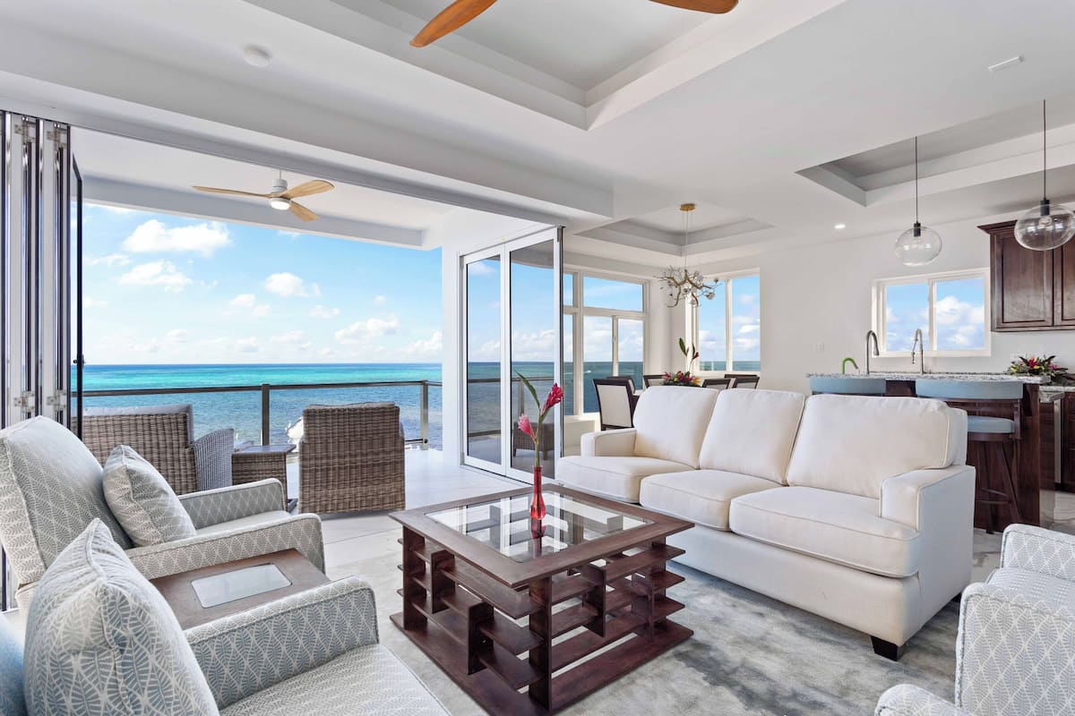 Een ruime woonkamer met een balkon met uitzicht op de oceaan, een witte bank en een houten bijzettafeltje.