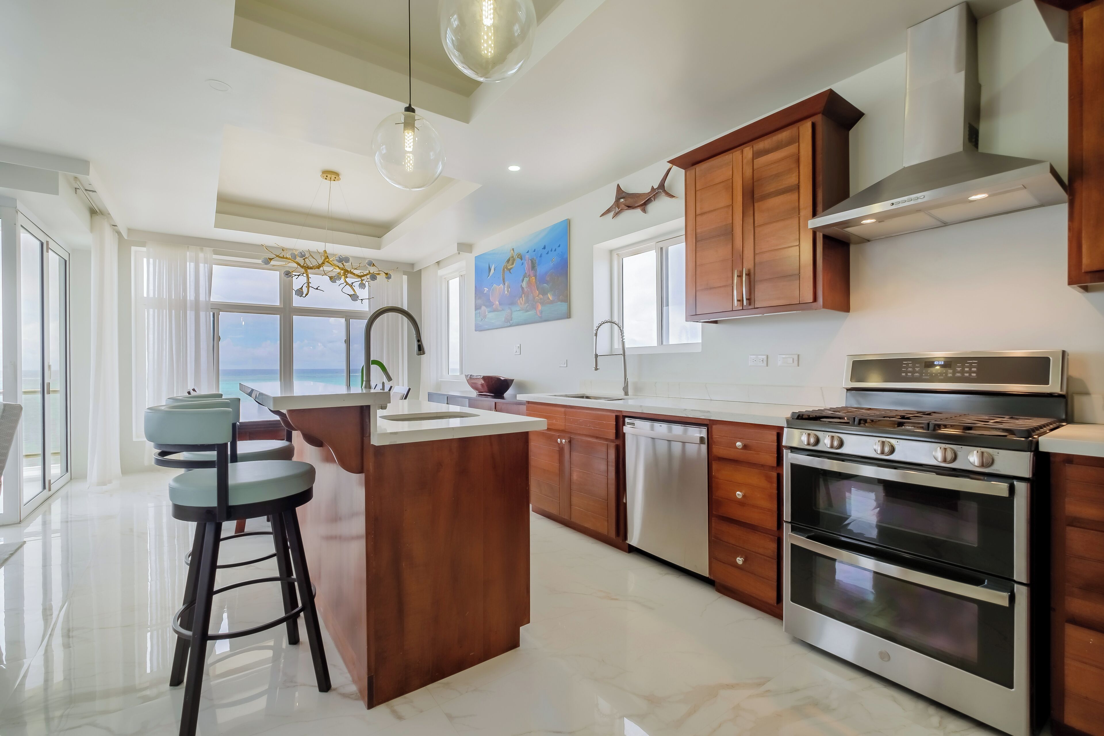 A modern kitchen with a central island, stainless steel appliances, wooden cabinets, and a large window offering a view.