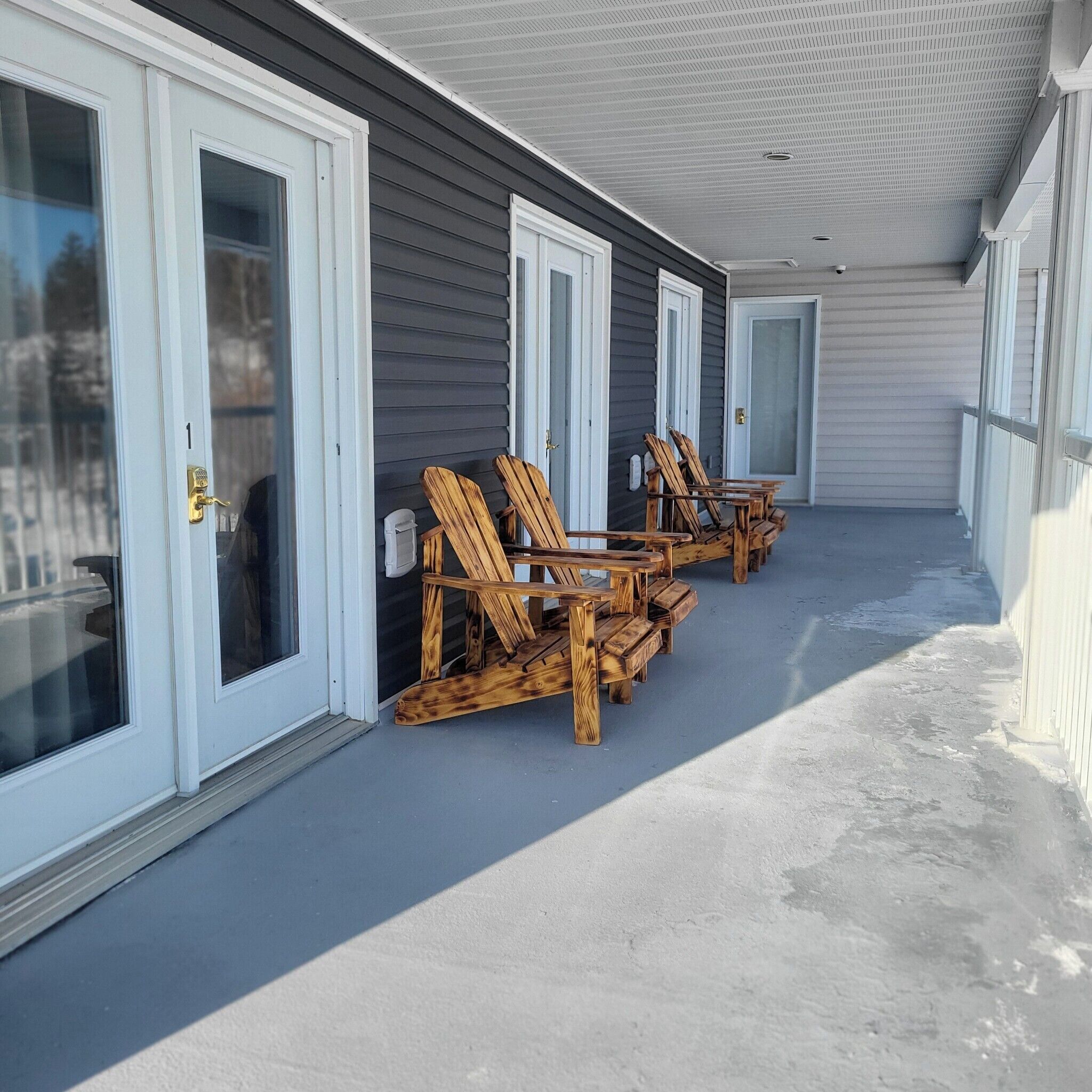A covered outdoor area with wooden Adirondack chairs and a concrete floor.