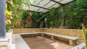 A covered outdoor area with a curved bench, surrounded by lush greenery and a brick wall. - Your cofortable Oasis in Playa del Carmen (Playa del Carmen)