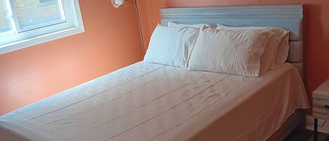A bedroom with a bed, a nightstand, a lamp, and a window.