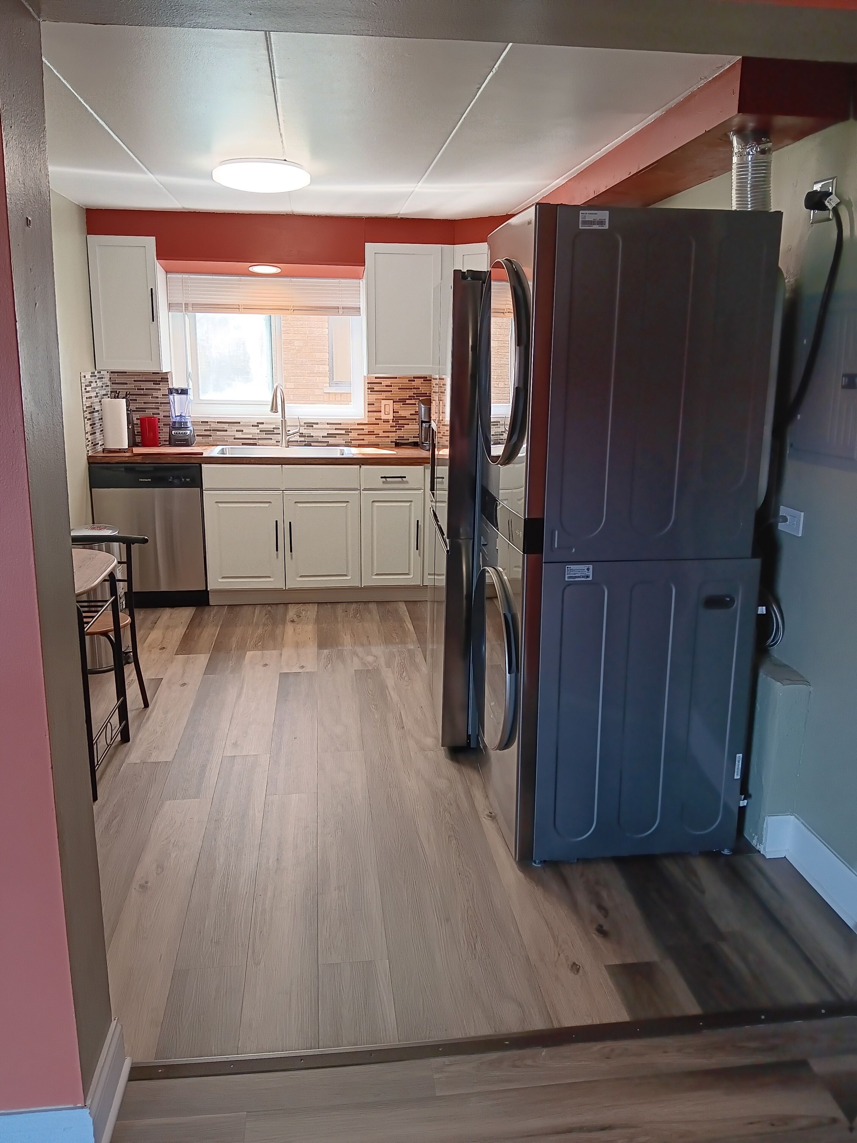 A modern kitchen with white cabinets, a black refrigerator, and a wooden floor.