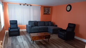 A living room with a sectional sofa, two armchairs, a coffee table, and a large window with blinds.