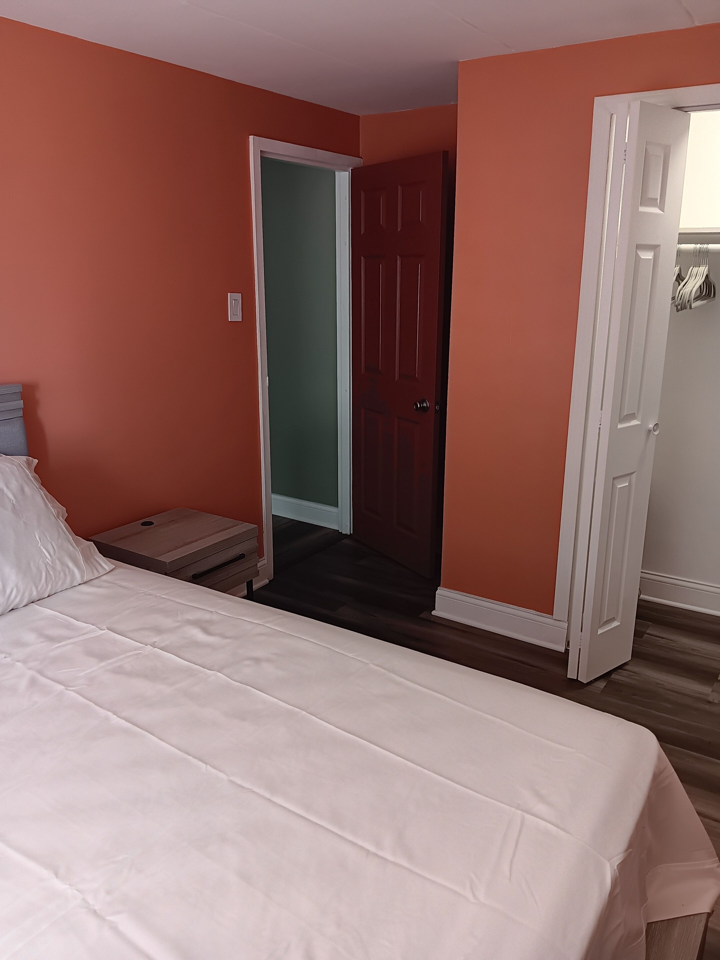 Une chambre à coucher avec un lit, une table de chevet, une porte rouge et un couloir.