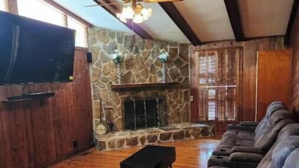 Un salón espacioso con chimenea de piedra, vigas de madera, un sofá grande y un televisor.