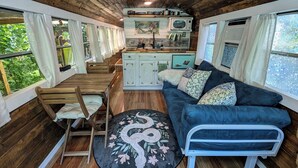 A cozy cabin interior with a wooden ceiling, a kitchenette, a sofa, and a dining area.