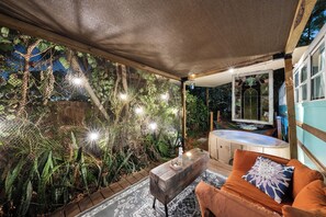 Un área de estar al aire libre con mesa de madera, cojines naranja y un jacuzzi.