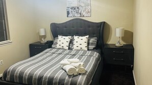A neatly made bed with striped bedding and rolled towels, two bedside tables with lamps, and a wall with framed artwork.
