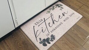 A kitchen with white cabinets, two sinks, and a countertop. There is a roll of paper towels and a doormat with the text "this kitchen is seasoned with love."
