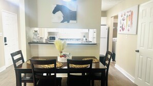 A dining area with a table set for four, surrounded by chairs. A decorative vase with dried plants is on the table.