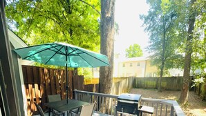 A wooden deck with a table and chairs, a barbecue grill, and a green umbrella.