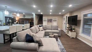 A modern living room with a sectional sofa, a dining area, and a TV mounted on the wall. - Enjoy creating beautiful memories at Sierra Stables Country Hideaway in 2026 (Langley Township)
