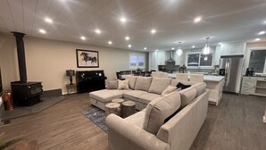 A modern living room with a sectional sofa, a fireplace, and a kitchen in the background. - Enjoy creating beautiful memories at Sierra Stables Country Hideaway in 2026 (Langley Township)
