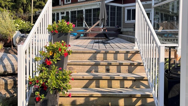 A wooden staircase with white railings leading to a covered outdoor area with a pool, surrounded by a house with large windows and a red brick exterior. - Enjoy creating beautiful memories at Sierra Stables Country Hideaway in 2026 (Langley Township)