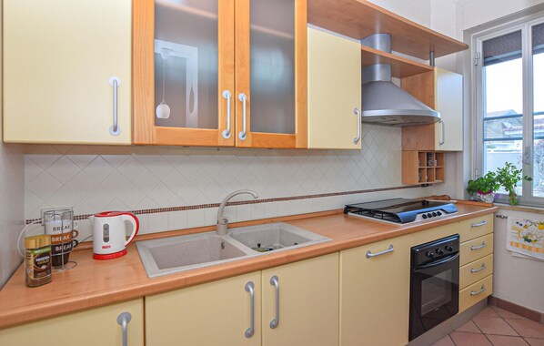 Une cuisine avec des meubles en bois, un évier en acier inoxydable, une cuisinière et une fenêtre donnant sur l’extérieur.