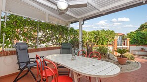 Un patio con una mesa y sillas blancas, rodeado de follaje y un muro de ladrillo.