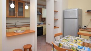 Cocina compacta con armarios de madera, un lavamanos, estufa y refrigerador. Hay una zona de comedor con una mesa y sillas.