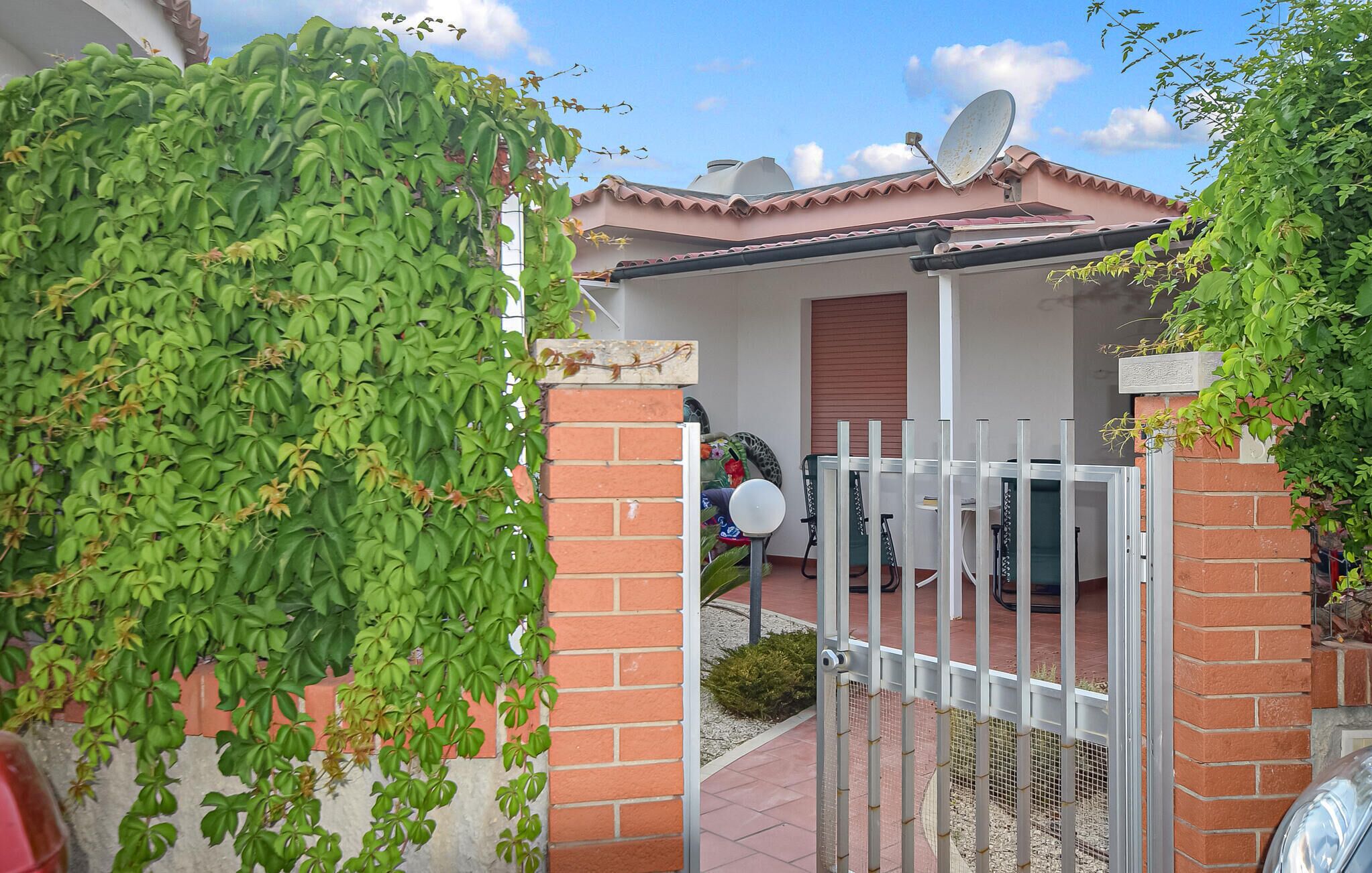A gated entrance with a brick wall and a metal gate, leading to a covered patio area with a satellite dish on the roof.