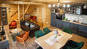 Un interior de cabaña acogedor, con una escalera de madera, un comedor con mesa y sillas, una cocina con electrodomésticos modernos y una sala de estar con sofá y cojines.