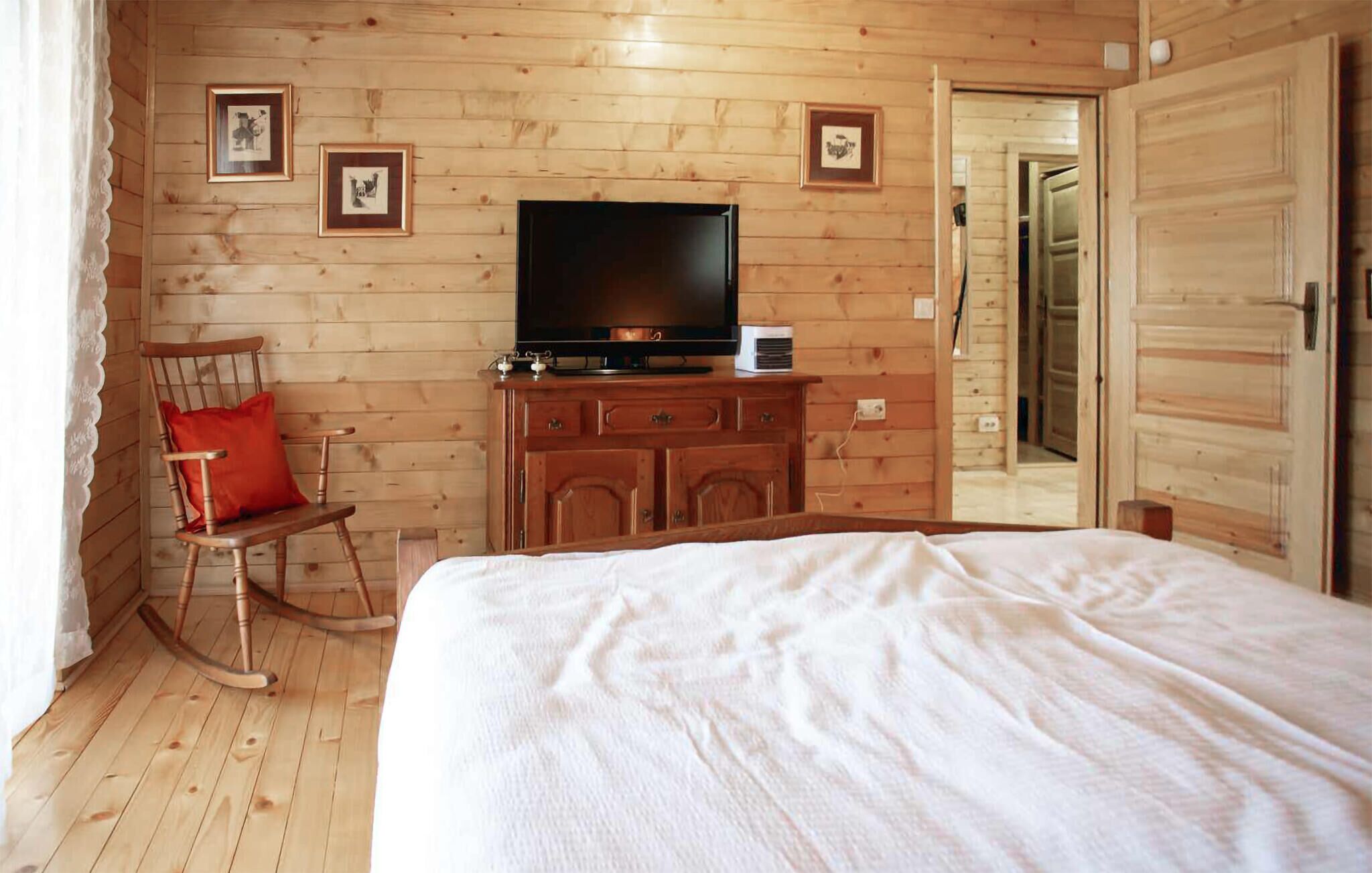 Una camera in legno con un letto, una poltrona a dondolo, una televisione su un mobile in legno e quadri appesi alle pareti.