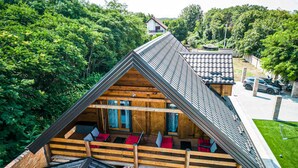 Una cabaña de madera con techo inclinado, un balcón y vistas a una carretera y vegetación.