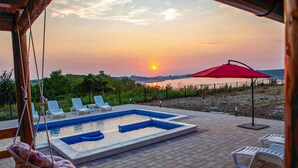 Una piscina con sillones de descanso y una sombrilla roja, frente a una vista de atardecer.