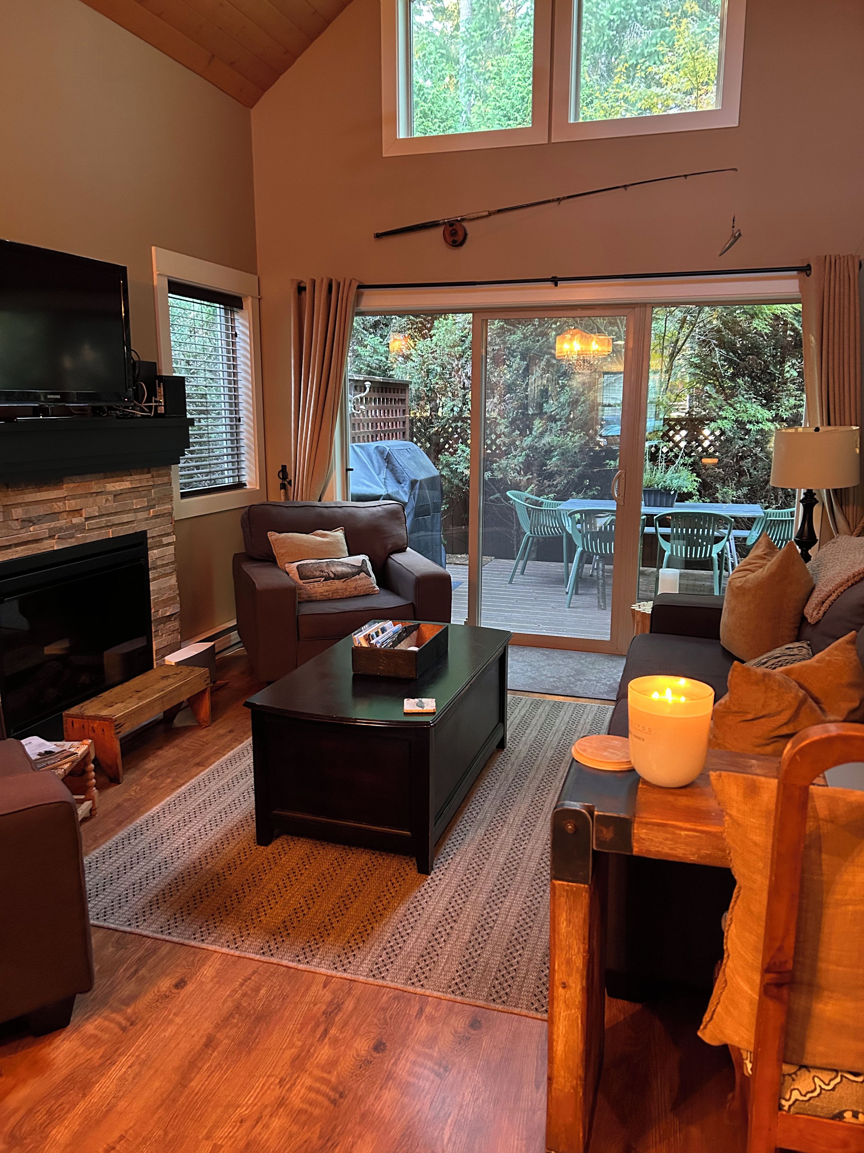 Un salon chaleureux avec une cheminée, des fauteuils confortables, une table basse et une vue sur l’extérieur grâce à de grandes portes-fenêtres coulissantes.