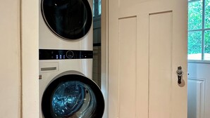 A laundry room with two stacked front-loading washing machines and a white door with a coat rack. - Family-friendly, Uptown New Orleans retreat, 4 blocks from St. Charles.  (New Orleans)