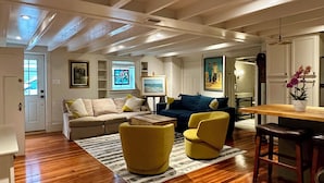 A spacious living room with wooden flooring, a beige sectional sofa, yellow armchairs, and a dining area with a wooden table and bar stools. - Family-friendly, Uptown New Orleans retreat, 4 blocks from St. Charles.  (New Orleans)