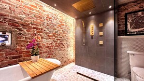 A bathroom with a brick wall, a wooden bench, a shower with a handheld showerhead, and a toilet. - Family-friendly, Uptown New Orleans retreat, 4 blocks from St. Charles.  (New Orleans)