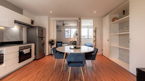 A modern kitchen with a built-in oven, a refrigerator, and a dining area with a round table and blue chairs. - Paradise found. Unique apartment in Playa del Carmen for you (Playa del Carmen)