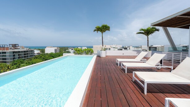 A rooftop pool with white lounge chairs, palm trees, and a view of the ocean. - Paradise found. Unique apartment in Playa del Carmen for you (Playa del Carmen)